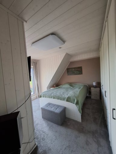 Schlafzimmer mit schrägem Dach, Bett, Nachttisch und grauer Sitzkiste.