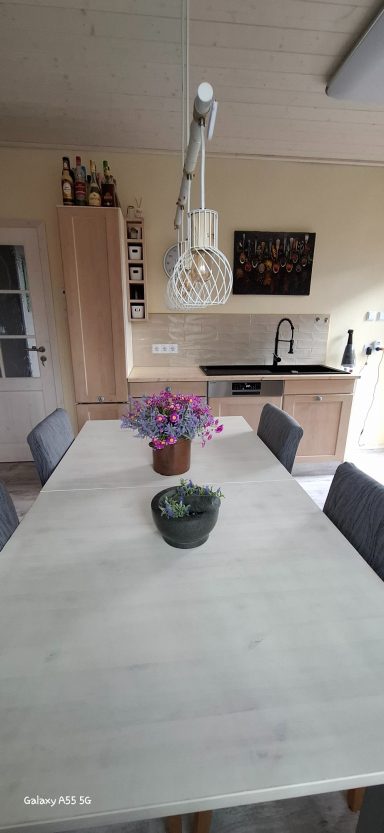 Heller Essbereich mit einem Tisch, Stühlen, einer Blumenvase und einer modernen Küchenzeile.