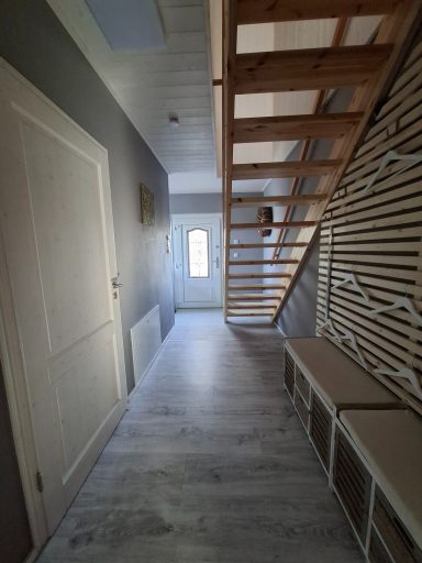Heller Flur mit Holztreppe, hellen Wänden und Tür zum Außenbereich.