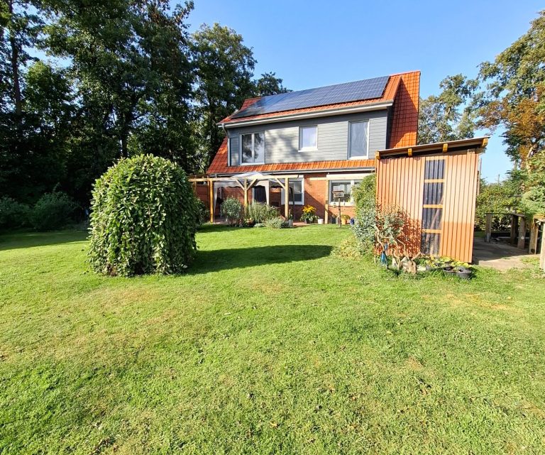 Modernes Haus mit Solarpanelen, umgeben von Garten und Bäumen.