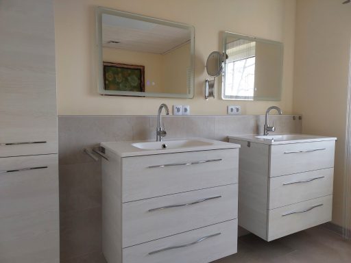 Moderne Badezimmer mit zwei weißen Waschtischen und großen Spiegeln.