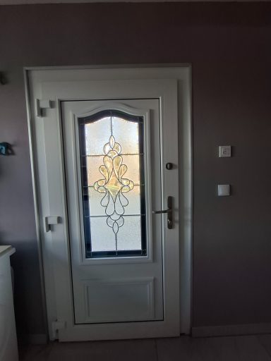 Weiße Tür mit Glasdetails und einem rechteckigen Fenster, an einer grauen Wand.