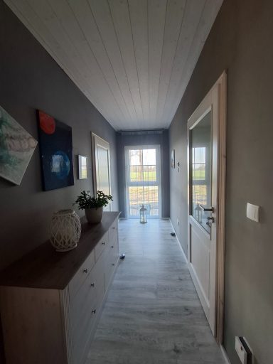 Langer Flur mit einem hellen Fenster, Kommode und Wandbildern an den Seiten.