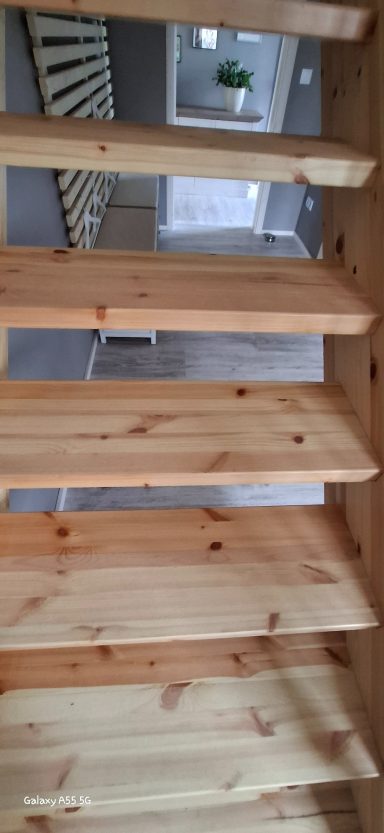Holzstufen einer Treppe mit einem Blick auf einen hellen Raum im Hintergrund.