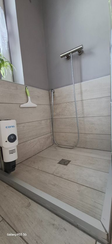 Geräumige, moderne Dusche mit Holzoptik und Wandhalterung für Handbrause.