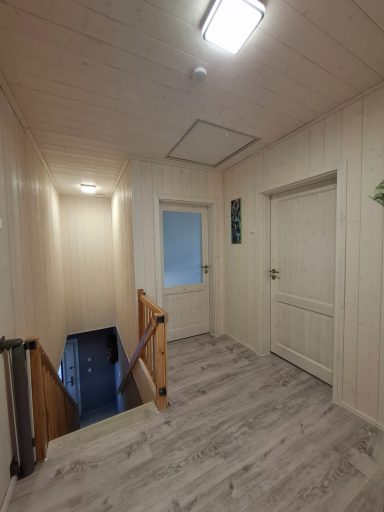Ein heller Flur mit Treppe, Türen und einem Fenster. Holzverkleidung und helle Wände.