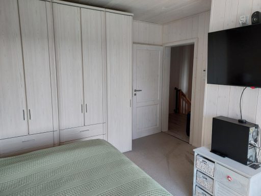 Schlafzimmer mit einem Bett, Schrank, Fernseher und weißer Wand.