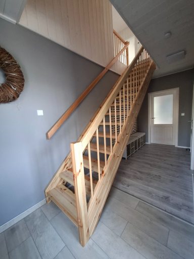 Holztreppe in einem modernen Flur mit grauen Wänden und Bodenbelag.