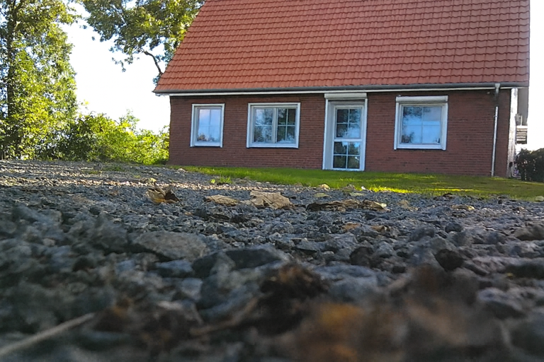 Kernsaniertes Einfamilienhaus in Oederquart Das Bild zeigt ein rotes Haus mit einem Satteldach und Fenstern, umgeben von Erde und Bäumen.