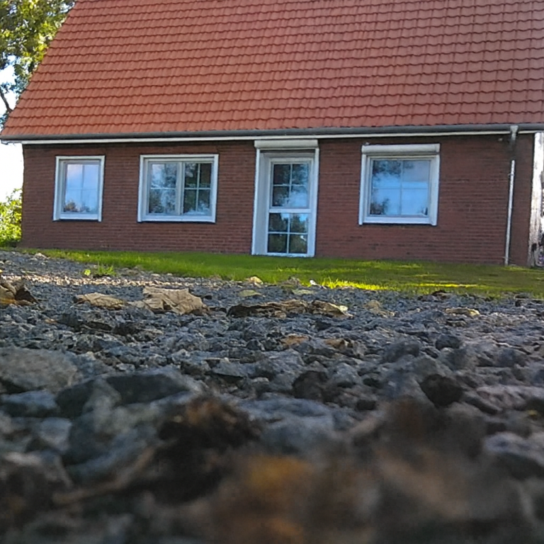 Ein rotes ziegelgedecktes Haus mit weißen Fenstern, umgeben von Land und Kies.