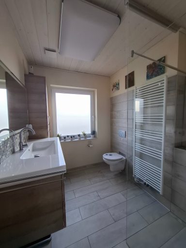 Helles Badezimmer mit Fenster, Waschbecken, WC und Dusche. Modernes Design.