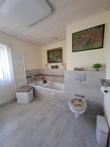 Heller Badezimmer mit Badewanne, WC und einem Fenster, dekoriert mit Pflanzen und Bildern.
